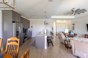 A modern kitchen with grey cabinets, a central island, and a dining area with chairs and a table.