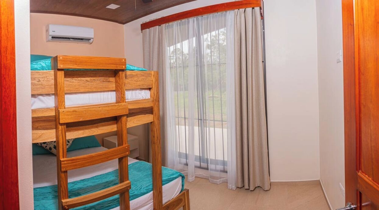 Ein Zimmer mit Etagenbetten, einem Fenster mit durchsichtigen Vorhängen und einer Klimaanlage an der Wand.