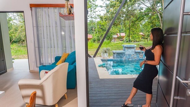 A modern living room with a pool area visible through an open door. - Hermosa Villa con Jacuzzi, e Hidromasaje en el Centro de la Fortuna (La Fortuna)