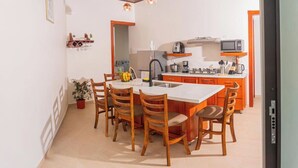 A compact kitchen with a central island, wooden chairs, and modern appliances. - Hermosa Villa con Jacuzzi, e Hidromasaje en el Centro de la Fortuna (La Fortuna)