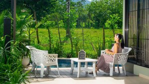 A patio with white chairs and a small table, surrounded by lush greenery and a pool. - Hermosa Villa con Jacuzzi, e Hidromasaje en el Centro de la Fortuna (La Fortuna)