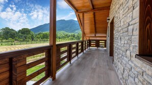 Une terrasse en bois couverte, dotée de murs en pierre, qui offre une vue sur un paysage verdoyant et des montagnes.