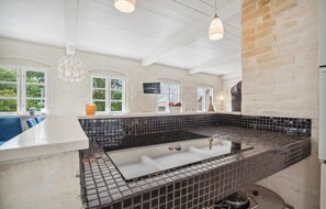 Una cocina moderna con salpicadero de azulejos negros, encimeras blancas y estufa integrada. Se ven ventanas con vistas a zonas verdes, y una lámpara colgante sobre la estufa.