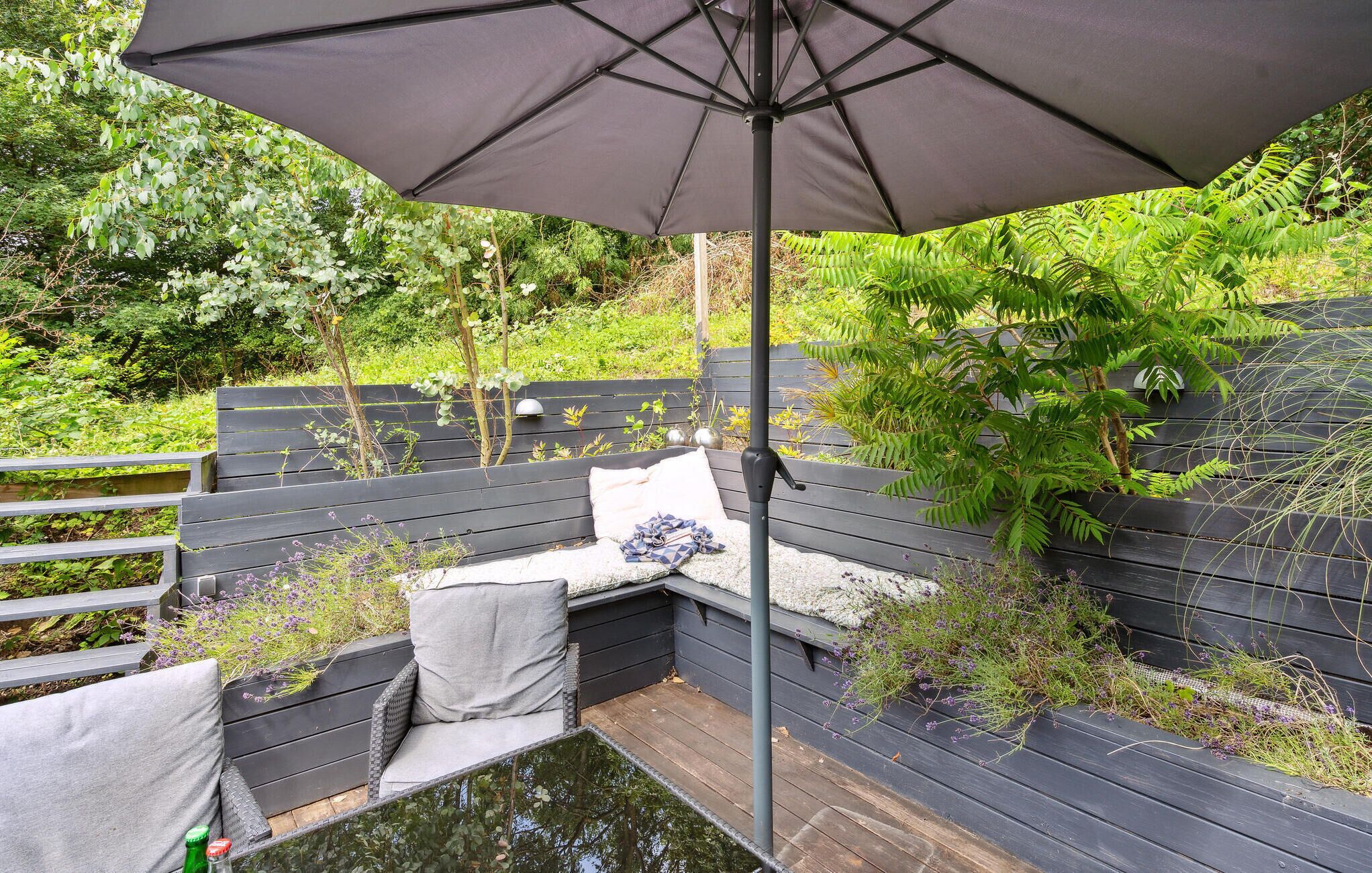 Een houten terras met een bank, een parasol en een kleine vijver.