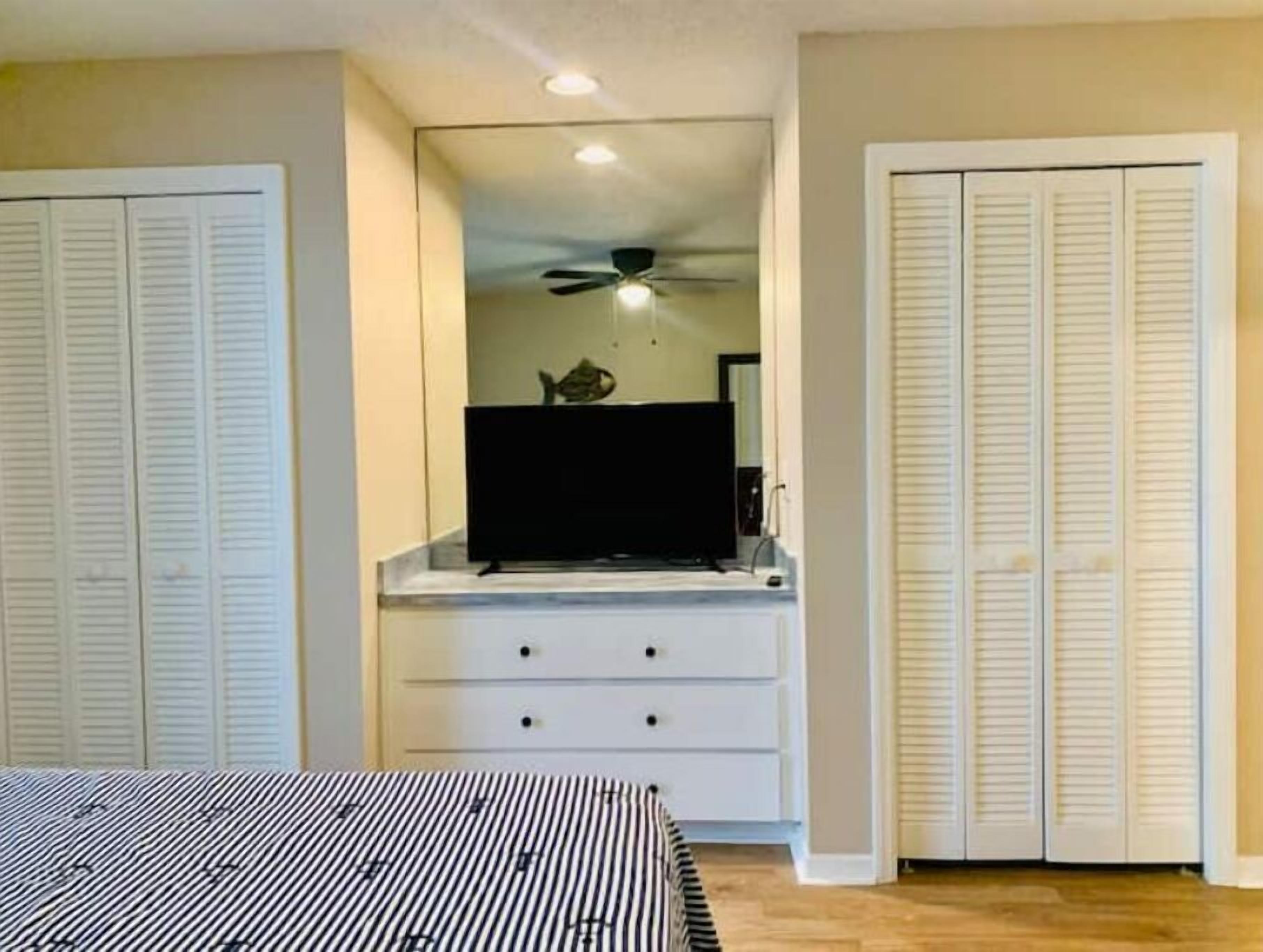 A bedroom with a bed, a dresser, a television on a stand, and a closet with louvered doors.