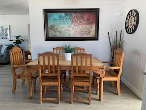 A dining area with a wooden table and chairs, a framed painting above the table, and a clock on the wall.