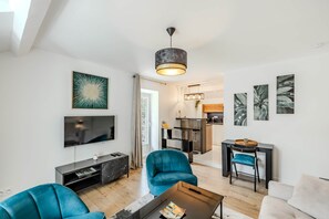 Ein modernes Wohnzimmer mit Fernseher, Türkis-farbenen Sesseln, einem Couchtisch und Kunstwerken an den Wänden.