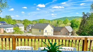 Una terraza de madera con una mesa y sillas, con vistas a una zona residencial con casas y un paisaje montañoso.