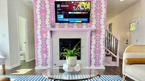 Una sala de estar con una televisión sobre la chimenea, una mesa de centro de vidrio y un libro, y una alfombra estampada.