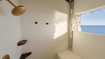 A bathroom with a shower, a window with a view of the sea, and a stone wall.