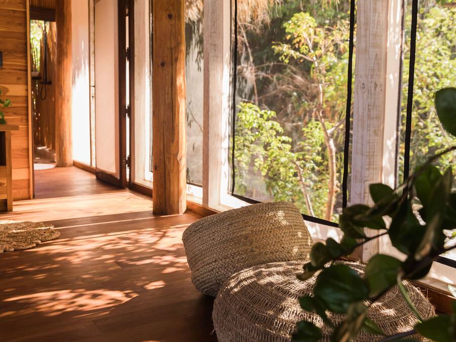 A wooden interior with large windows, a woven bench, and a thatched roof.