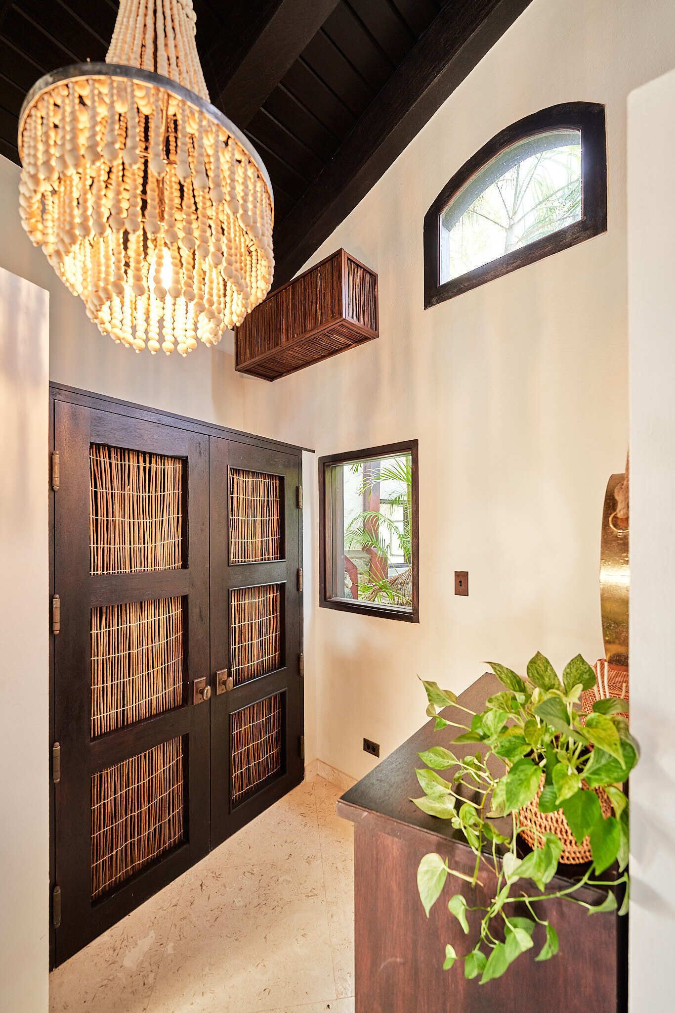 A hallway with a dark wooden door, a large chandelier, a small window, and a potted plant.