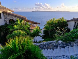 Vista costera con una escalera de piedra que lleva a un edificio con techo de paja, con vistas al mar.