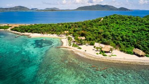 An aerial view of a tropical island with clear turquoise waters, a sandy beach, and lush greenery. - The Aerial, BVI (East End)