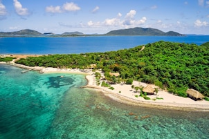 Vista aérea de una isla tropical con aguas turquesas cristalinas, una playa arenosa y exuberante vegetación.