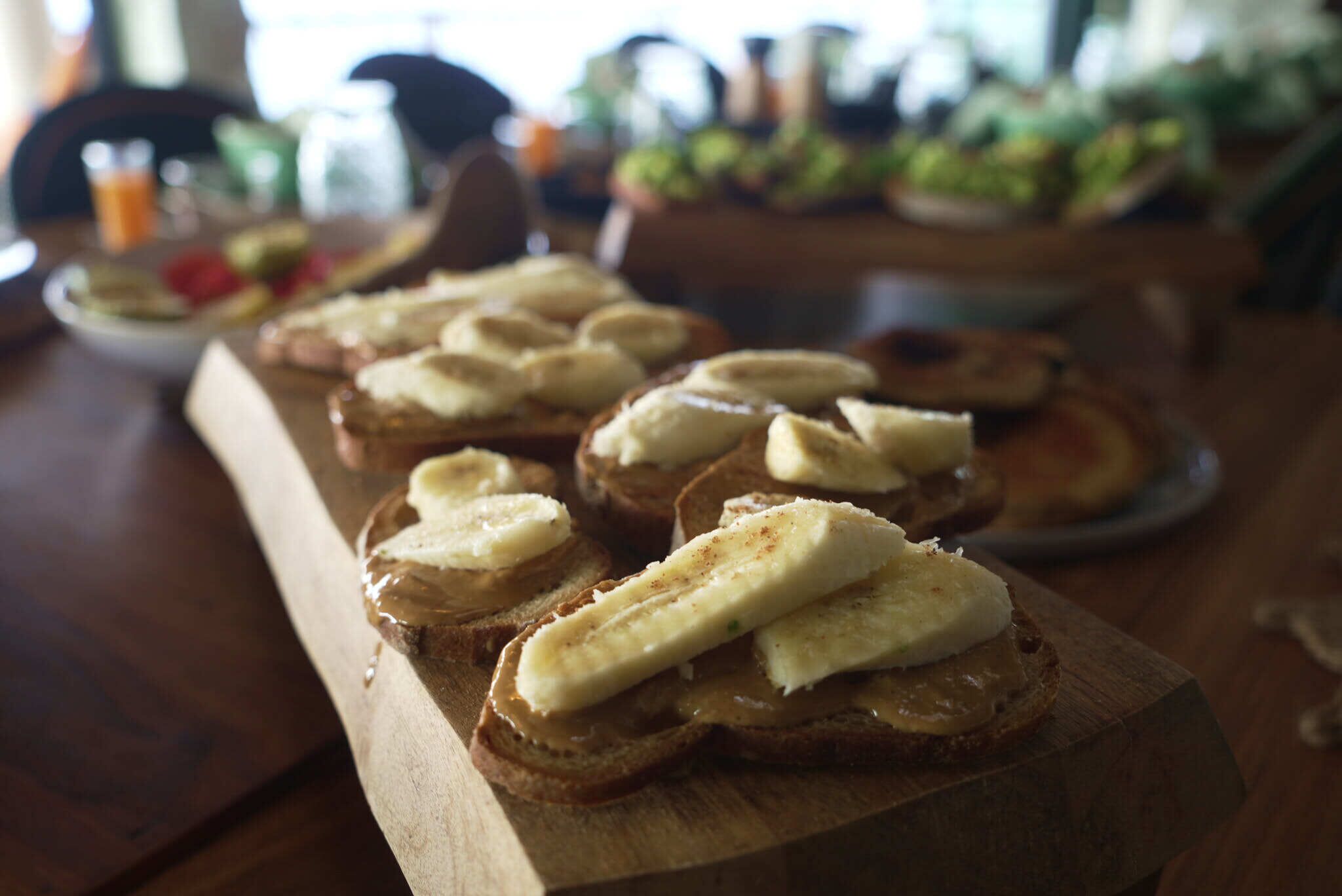 A wooden board with several pieces of toast topped with banana slices and spread.