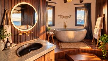 A bathroom with a large freestanding bathtub, wooden paneling, a round mirror, and a view of the sea.