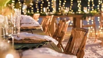 Un área de comedor al aire libre con luces colgantes, sillas de madera y una mesa preparada para una comida.