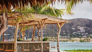 A beachside swing set with a concrete base, surrounded by palm trees and a view of a coastal town. - The Aerial, BVI (East End)