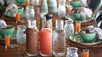 A long dining table set with green bowls, glasses, and bottles of beverages, with a woven placemat in the center.