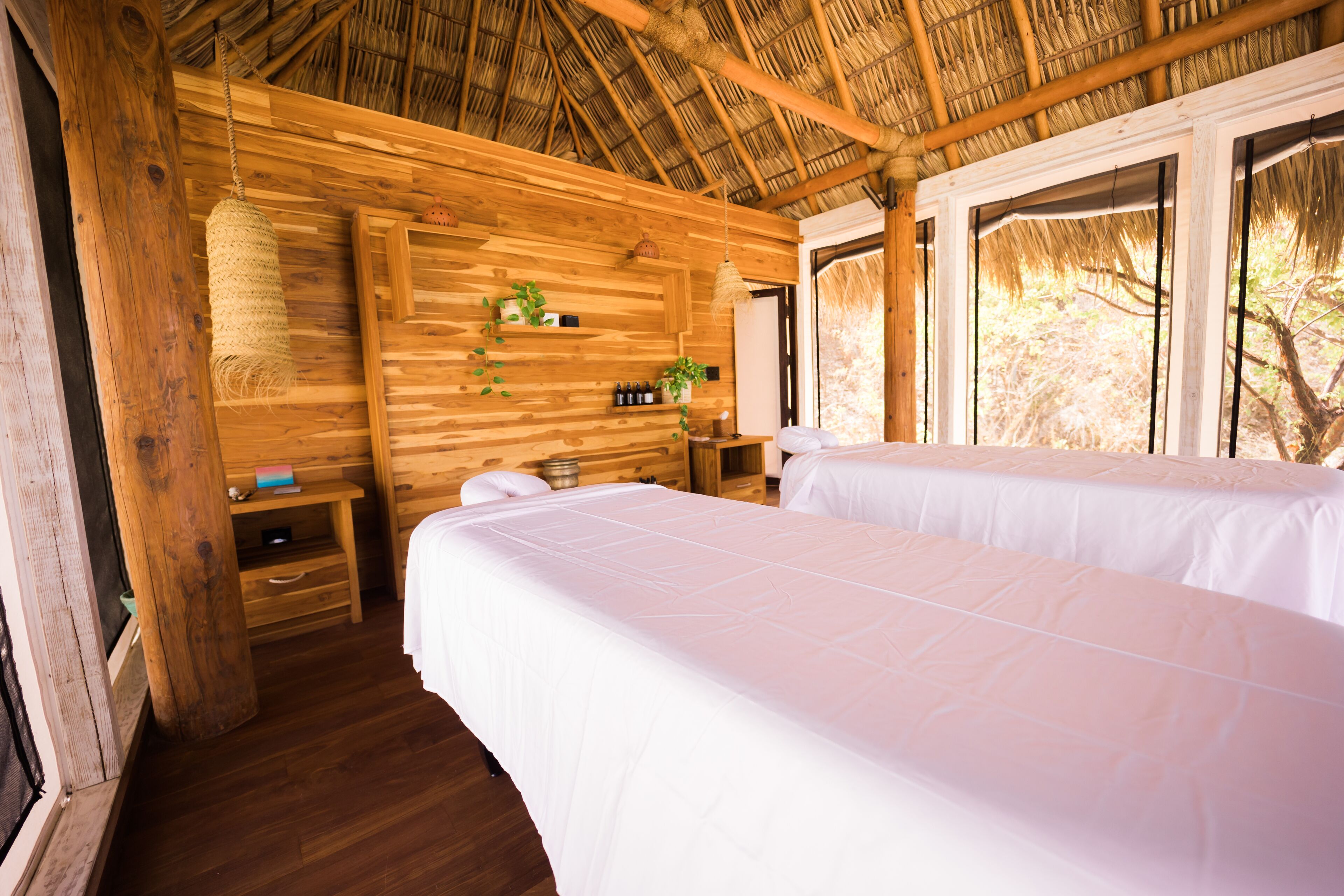 Ein Zimmer aus Holz mit zwei Betten, einem Pflanzenregal und einem Fenster.