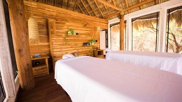 Ein Zimmer aus Holz mit zwei Betten, einem Pflanzenregal und einem Fenster.