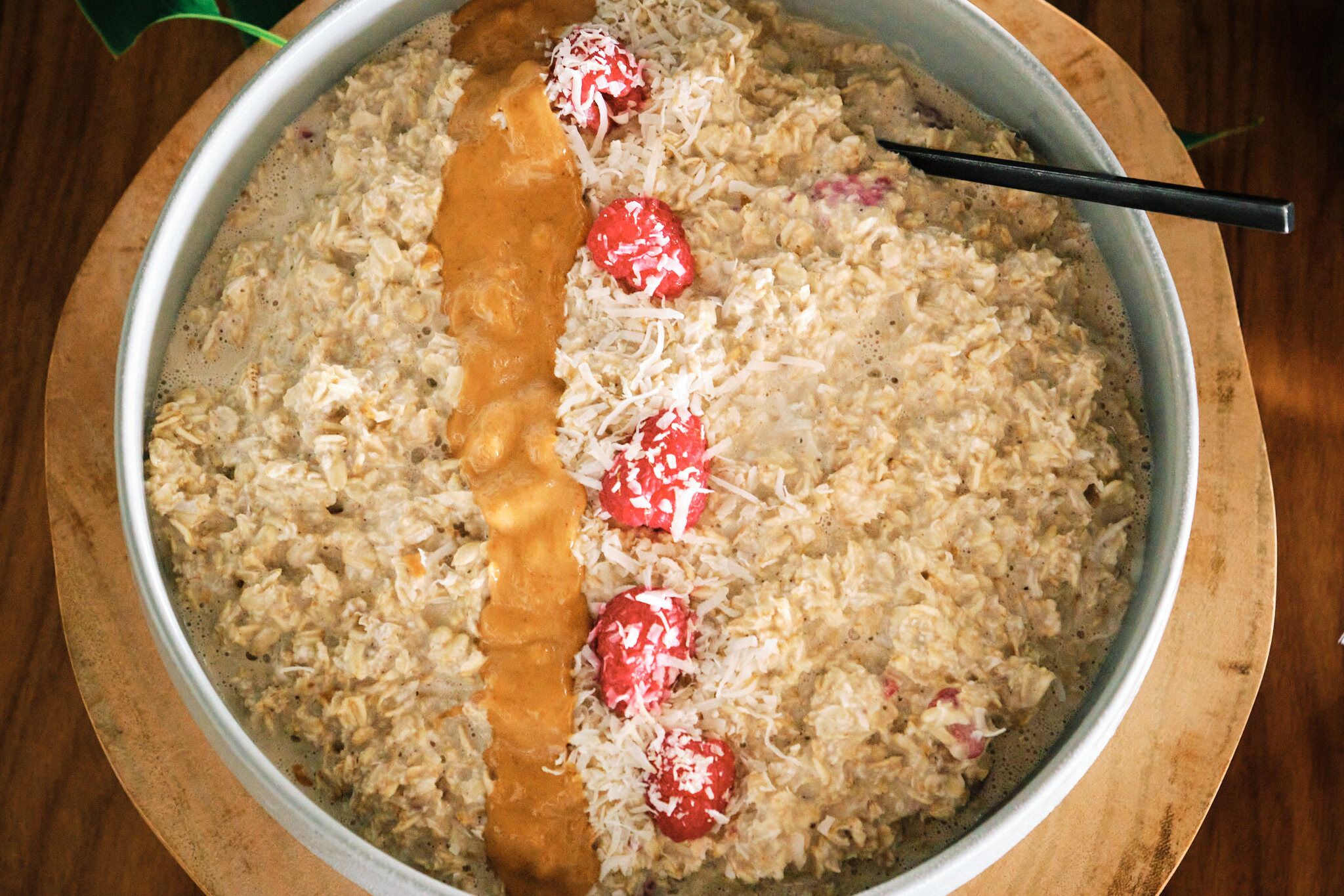 Un tazón de avena con bayas rojas y una cucharada de mantequilla de maní.