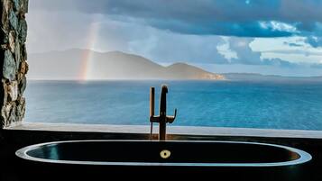 A bathtub with a view of the sea and a rainbow.
