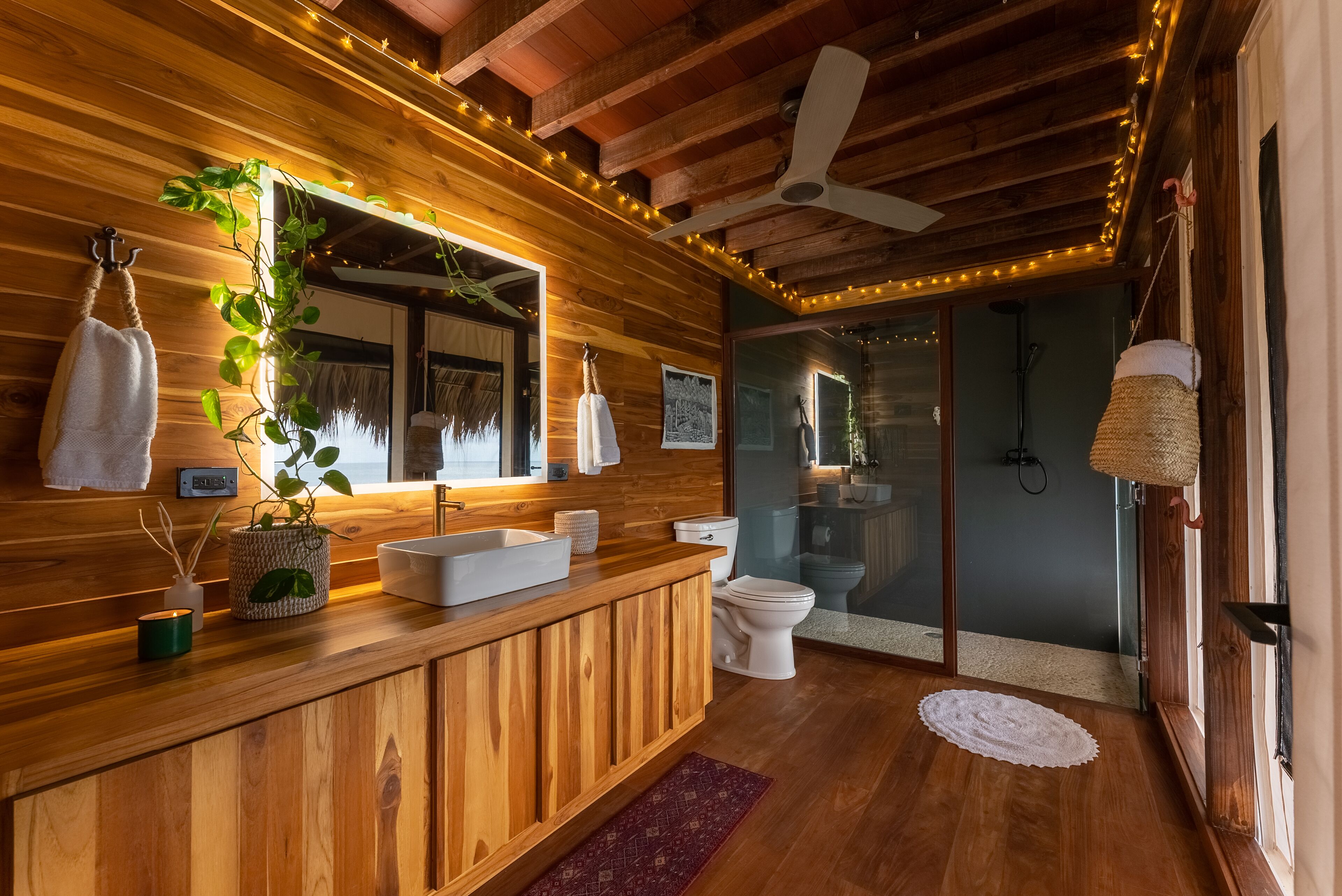Un interior de madera con tocador de madera, un lavabo blanco, un inodoro y una zona de ducha.