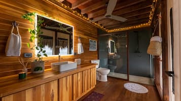 Un interior de madera con tocador de madera, un lavabo blanco, un inodoro y una zona de ducha.