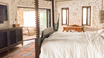 A spacious bedroom with a large bed, a wooden floor, a hanging chair, and a view of the outdoors.