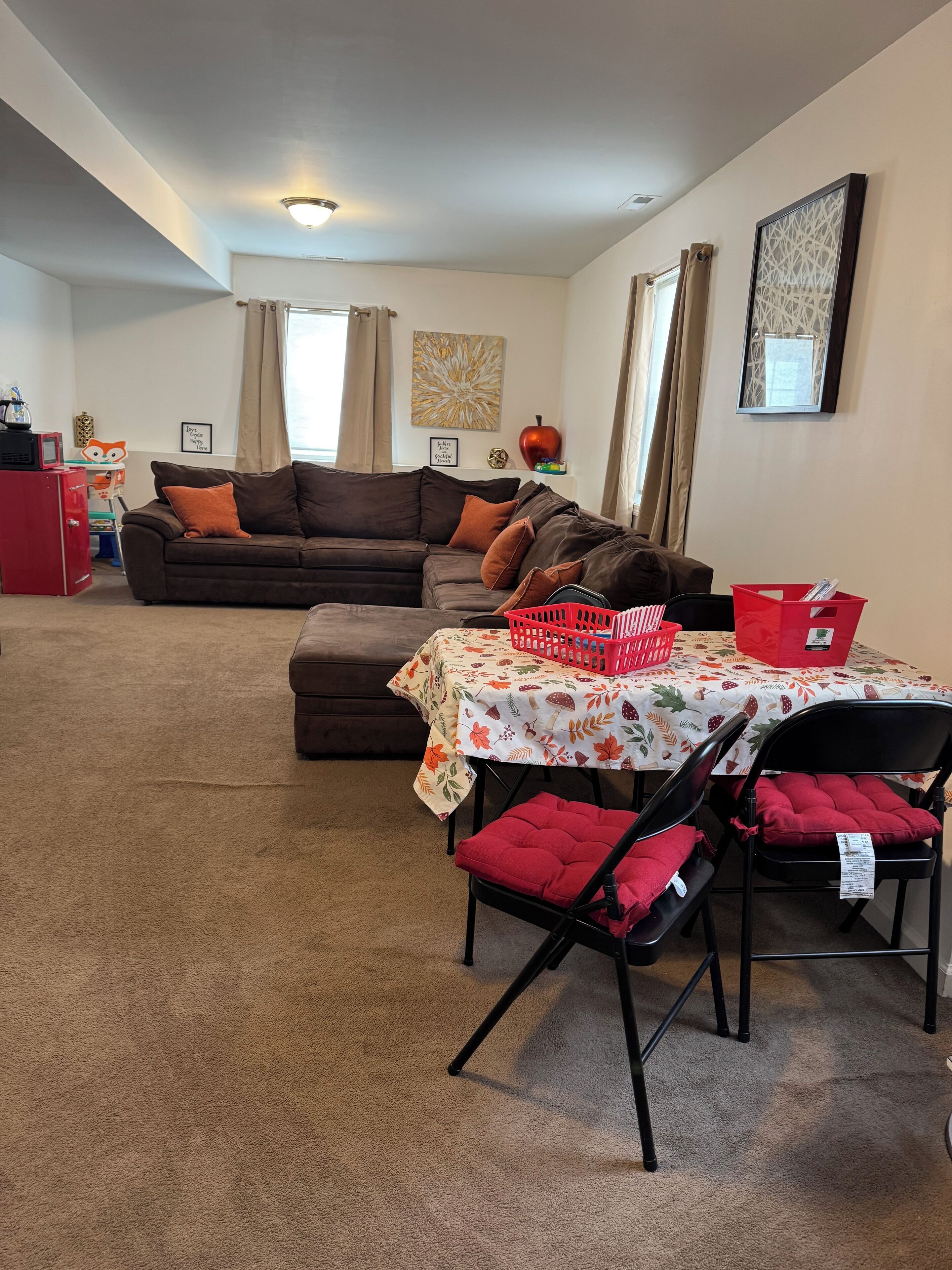 Una sala de estar con un sofá marrón, una mesa de comedor con mantel floreado y una cesta roja.