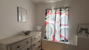 Una habitación con un aparador blanco, una ventana con cortina, un cuadro en la pared y un adorno pequeño sobre el aparador.