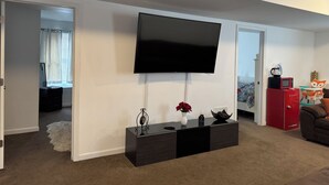 Una sala de estar con un televisor de pantalla plana montado en la pared, un mueble negro para entretenimiento con un jarrón de flores rojas, y un armario rojo con una cafetera encima.