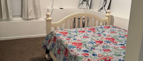 Un dormitorio con cama, televisor de pantalla plana, ventana con cortinas e imagen colgada en la pared.