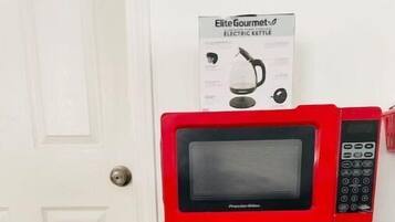 Un réfrigérateur rouge avec un four à micro-ondes sur le dessus, une poignée de porte et le nom de la marque.