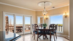Un comedor con una mesa y sillas, una araña y ventanas grandes con vistas.