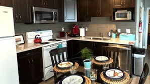 A modern kitchen with dark wood cabinets, stainless steel appliances, and a glass dining table set with plates and cutlery. - White Rock Beach Getaway (White Rock)