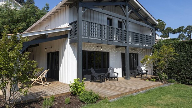 A two-story house with a balcony, wooden deck, and outdoor seating area.