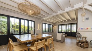 A spacious dining area with a wooden table and chairs, large windows, and a ceiling fan.