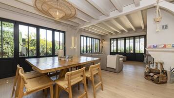 A spacious dining area with a wooden table and chairs, large windows, and a ceiling fan.
