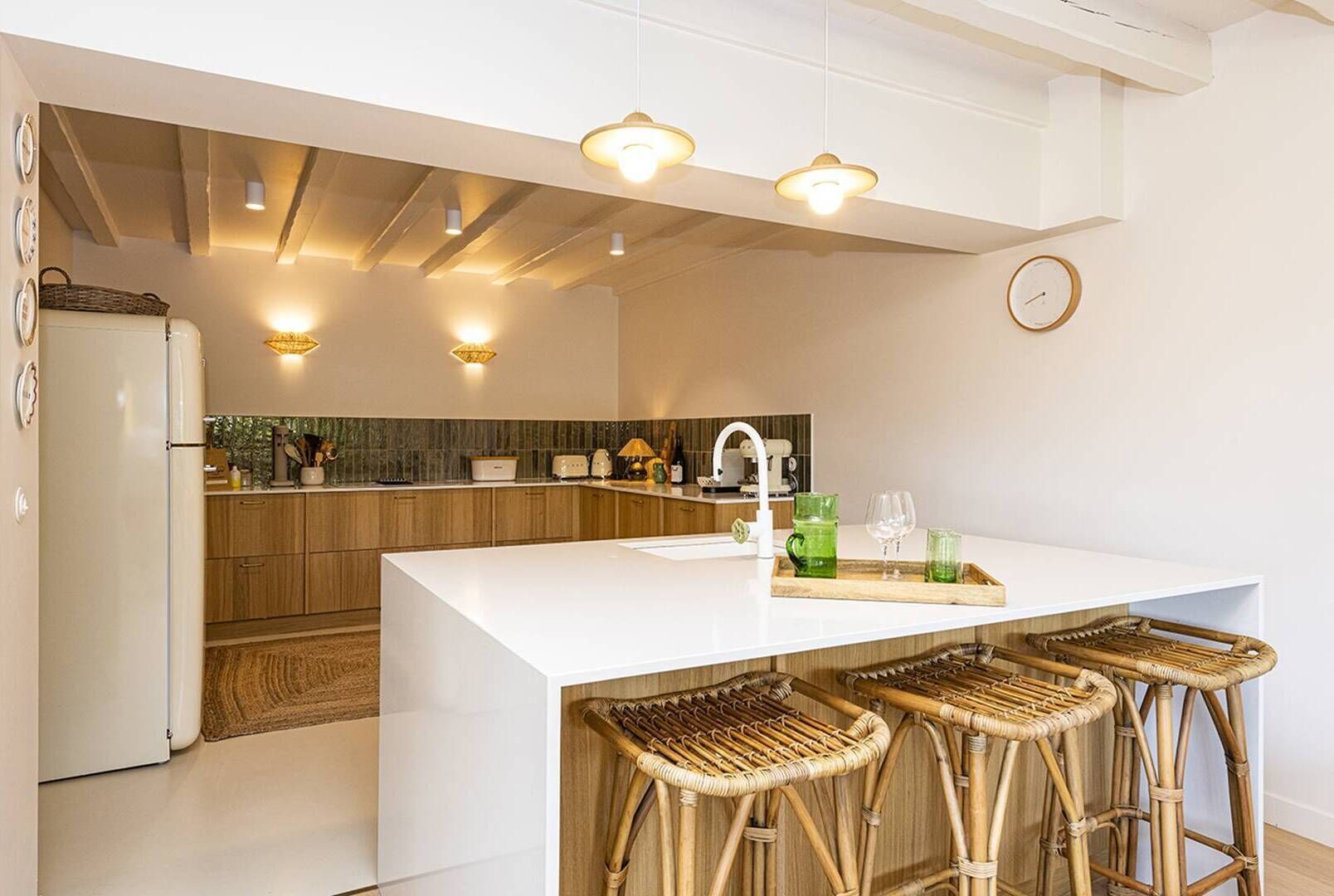 A modern kitchen with a central island, bar stools, and a hanging light fixture.
