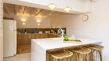 A modern kitchen with a central island, bar stools, and a hanging light fixture.