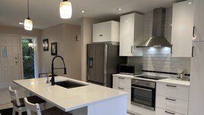 Une cuisine moderne avec des meubles blancs, des appareils en acier inoxydable et des luminaires suspendus.