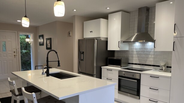 A modern kitchen with white cabinetry, stainless steel appliances, and pendant lighting.