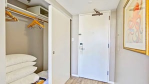 Un couloir avec une porte blanche, un placard rempli de vêtements et un tableau accroché au mur.
