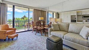 Une chambre d’hôtel avec balcon, un canapé, une table à manger avec des chaises et un coin cuisine.
