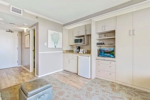 Compact kitchen with light-colored cabinetry, microwave, coffee maker, and TV.