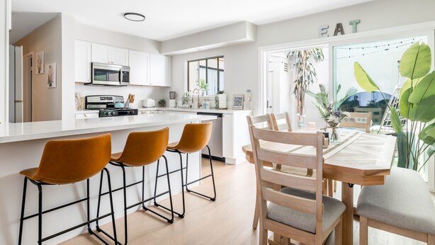 Una cocina moderna con armarios blancos, un microondas y un comedor con una mesa y sillas de madera.