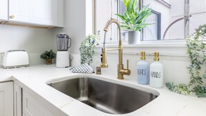 Una cocina moderna con un lavamanos de acero inoxidable, armarios blancos, un tostador, una licuadora y una planta en maceta junto a la ventana.
